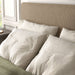 Left facing close up view of a modern light brown corduroy channel tufted headboard queen platform bed in a room with linens and accessories