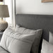 Left facing close up view of a modern dark grey corduroy channel tufted headboard queen platform bed in a room with linens and accessories