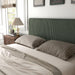 Left facing close up view of a modern green corduroy channel tufted headboard queen platform bed in a room with linens and accessories