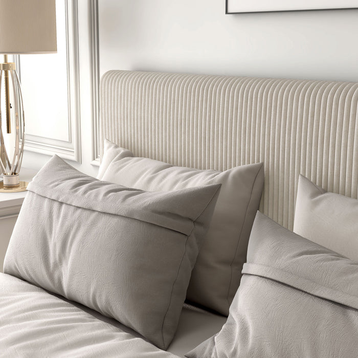 Left facing close up view of a modern ivory corduroy channel tufted headboard queen platform bed in a room with linens and accessories