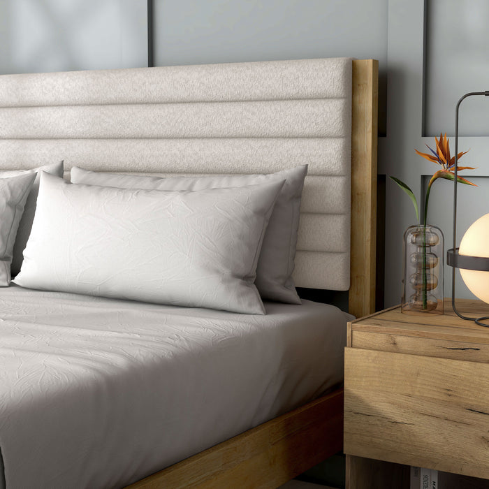 Left facing close up view of a modern wood frame queen platform bed with a channel tufted upholstered white boucle headboard in a room with linens and accessories