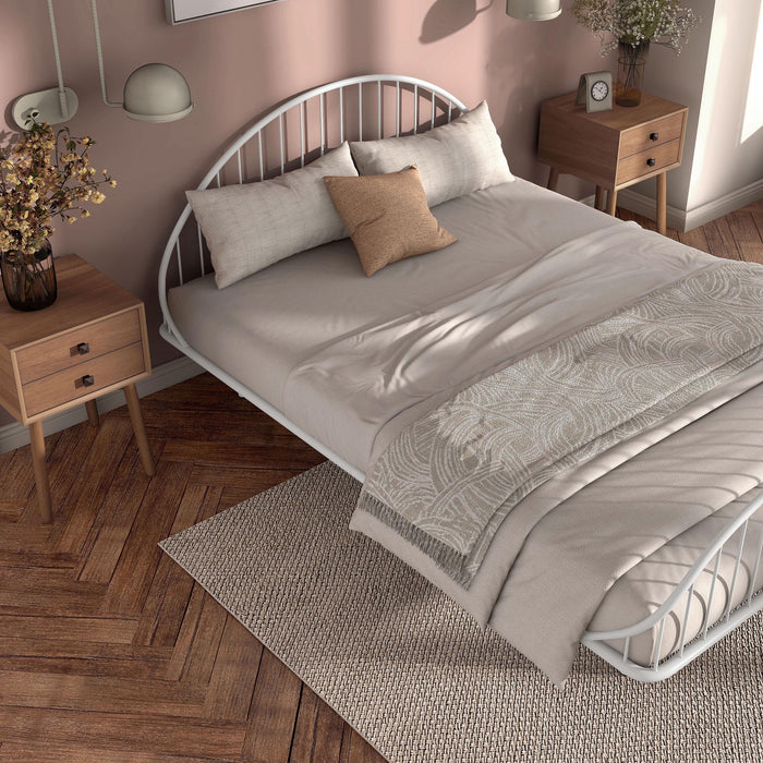 Left facing close up high-camera view of an industrial white metal queen bed frame with rounded head and footboards in a room with linens and accessories