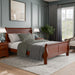 Right facing traditional cherry finish solid wood queen sleigh bed in a room with linens and accessories