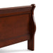 Right facing close up of a traditional cherry finish solid wood queen sleigh bed showing its sleigh footboard, on a white background