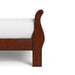 Front facing close up side view of a traditional cherry finish solid wood queen sleigh bed showing its footboard, on a white background