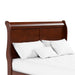 Right facing close up of a traditional cherry finish solid wood queen sleigh bed showing its sleigh headboard, on a white background