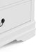 Right facing close up of a traditional white finish solid wood five-drawer chest showing its lower molded trim and bracket foot, on a white background