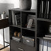 Right facing durable modern four-cubby black storage bookcase as part of a larger modular configuration in a room with accessories