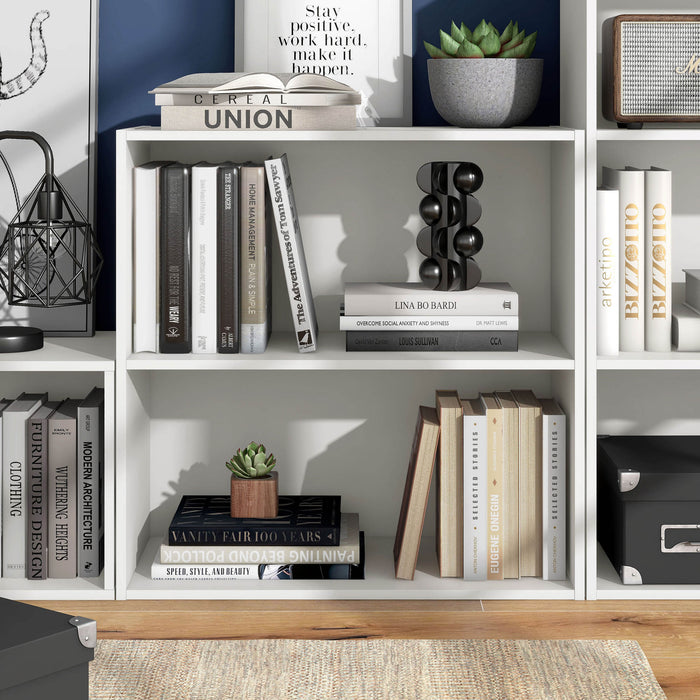 Front facing durable modern two-shelf white storage bookcase in a larger modular configuration in a room with accessories