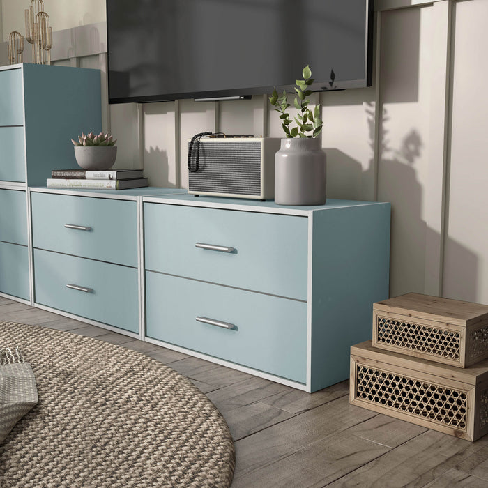 Left facing modern two-drawer light blue storage cabinet with silver handles in a larger modular bookcase in room with accessories