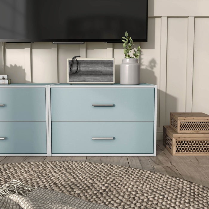 Front facing modern two-drawer light blue storage cabinet with silver handles in a larger modular bookcase in room with accessories