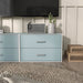 Front facing modern two-drawer light blue storage cabinet with silver handles in a larger modular bookcase in room with accessories