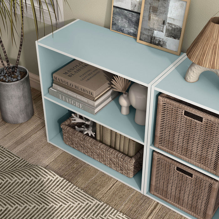 Left facing high-camera view of a durable modern two-shelf light blue storage bookcase in a larger modular configuration in a room with accessories