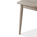 Left facing close up view of the corner and leg of a durable modern engineered wood rectangular dining table with a natural finish on a white background