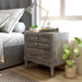 Left-angled transitional grey 2-drawer nightstand next to an upholstered grey bed. A grey geometric rug decorates the floor, while a window illuminates the books, succulents, and tea cup on the nightstand. 