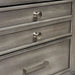 Detail shot of the drawer fronts of a transitional grey 2-drawer nightstand. The top drawer has a double-drawer facet with two silver knobs to contrast the lower drawer with a silver bar pull.